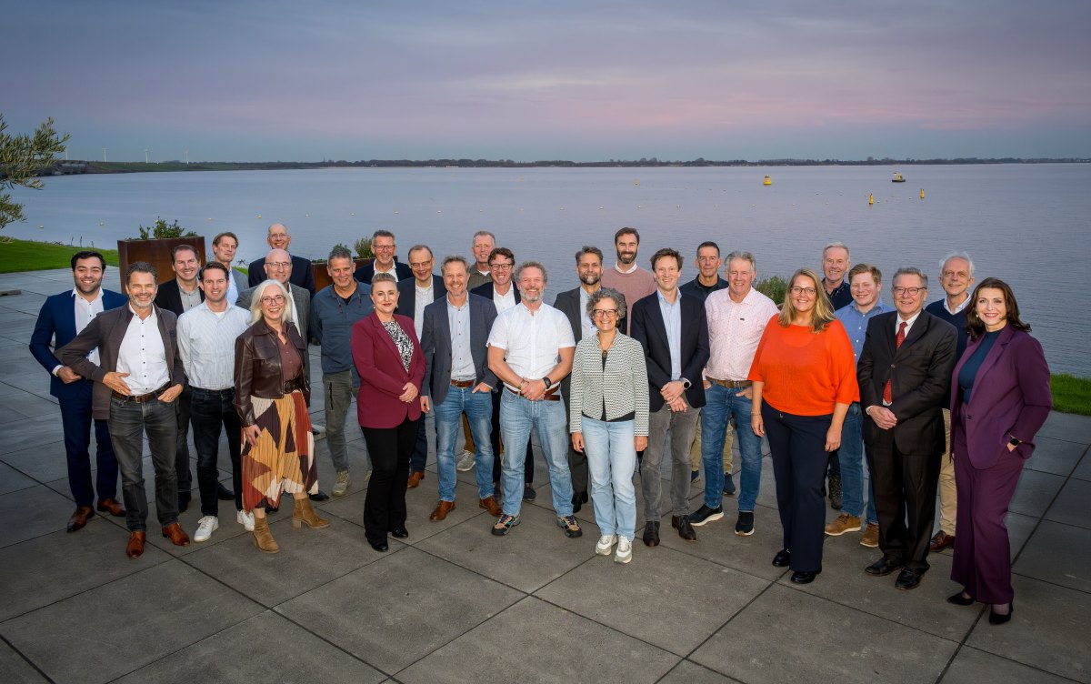 We zien een groep met vertegenwoordigers van de Delta21-leden staand poseren voor een horizon met water op de achtergrond.